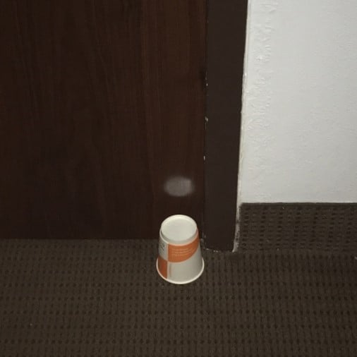 A small white and orange hotel paper cup is standing on the floor, right next to the hotel door's bottom.