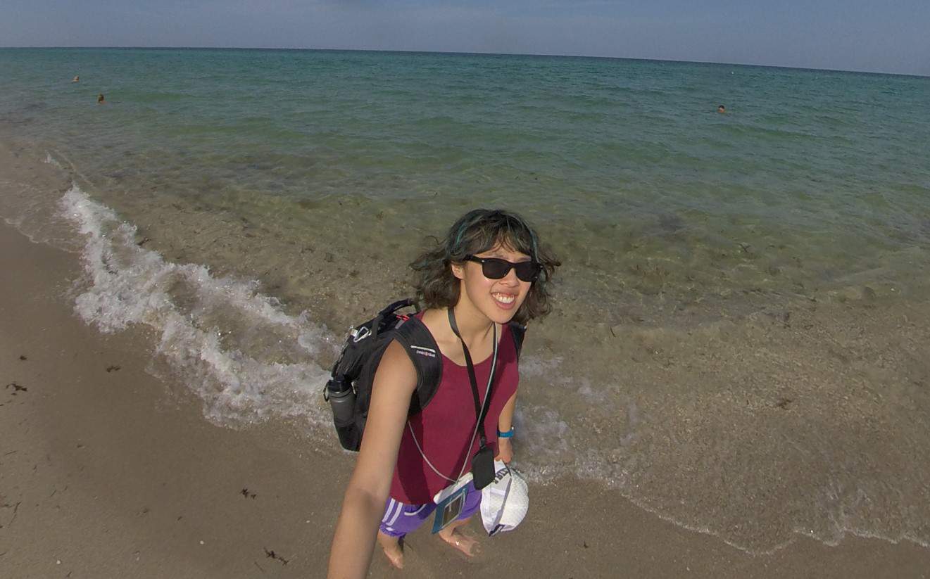 Meggie is standing on the wet sand next to the clear bright blue ocean. Hollywood North Beach Park in Fort Lauderdale-Hollywood, Florida, United States.