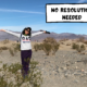 Meggie is wearing a white sweatshirt and purple pants. She is raising her arms in the sky and smiling. She is standing in the desert and sand dunes of Death Valley National Park in southern California, United States. A comic text box says, "no resolution needed."