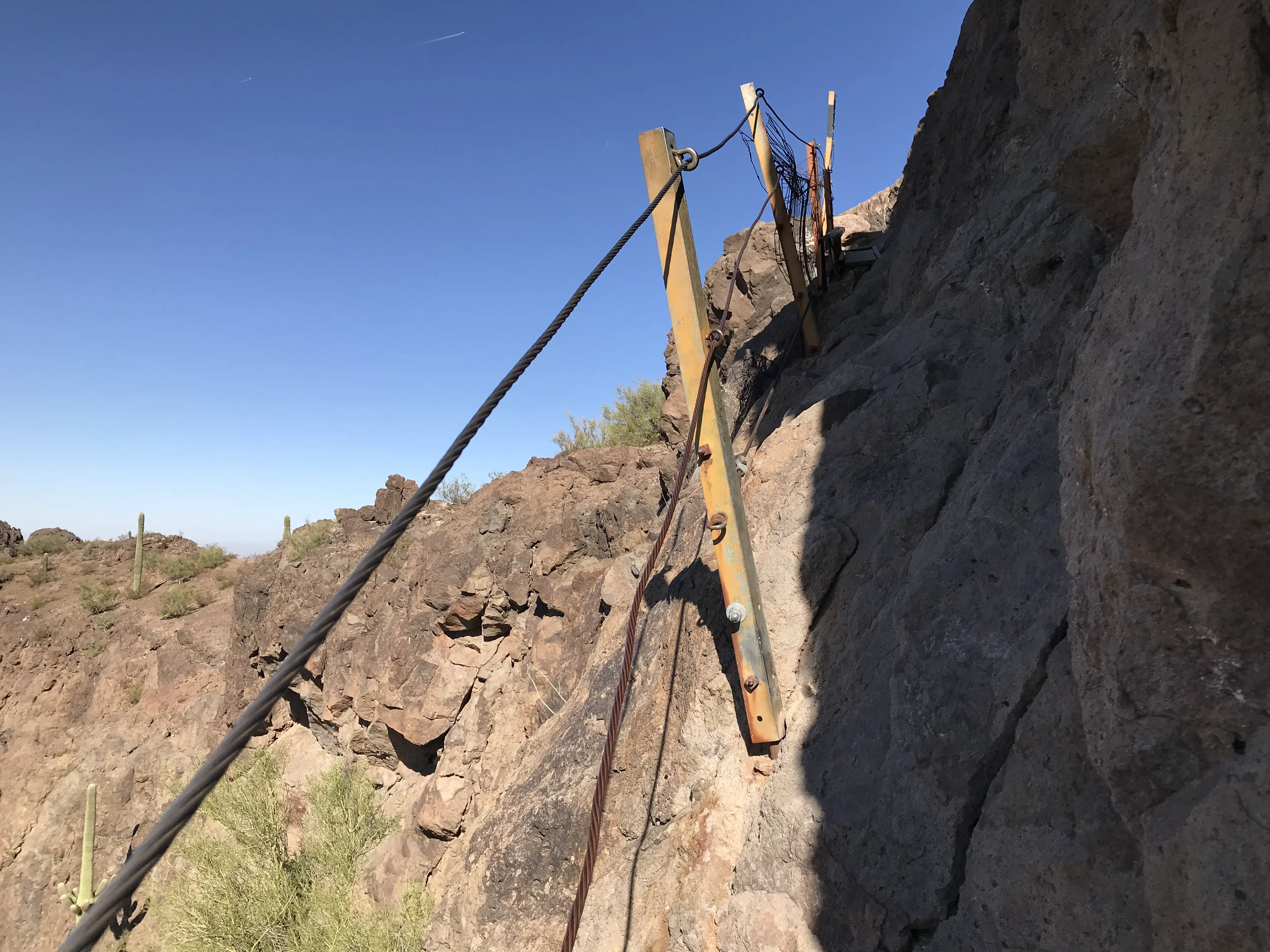Cables are jutting out along the steep brown mountainside. The other side of the cables is nothing but a tall scary drop down the mountain. In Picacho Peak State Park between Tucson and Phoenix, Arizona, United States.