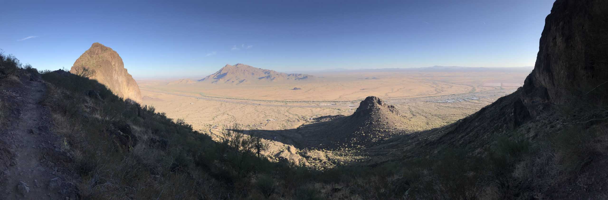 A panorama of the brown mountain range and brown desert below. Interstate 10 and the railroad tracks are visible. A clear blue sky. In Picacho Peak State Park between Tucson and Phoenix, Arizona, United States.