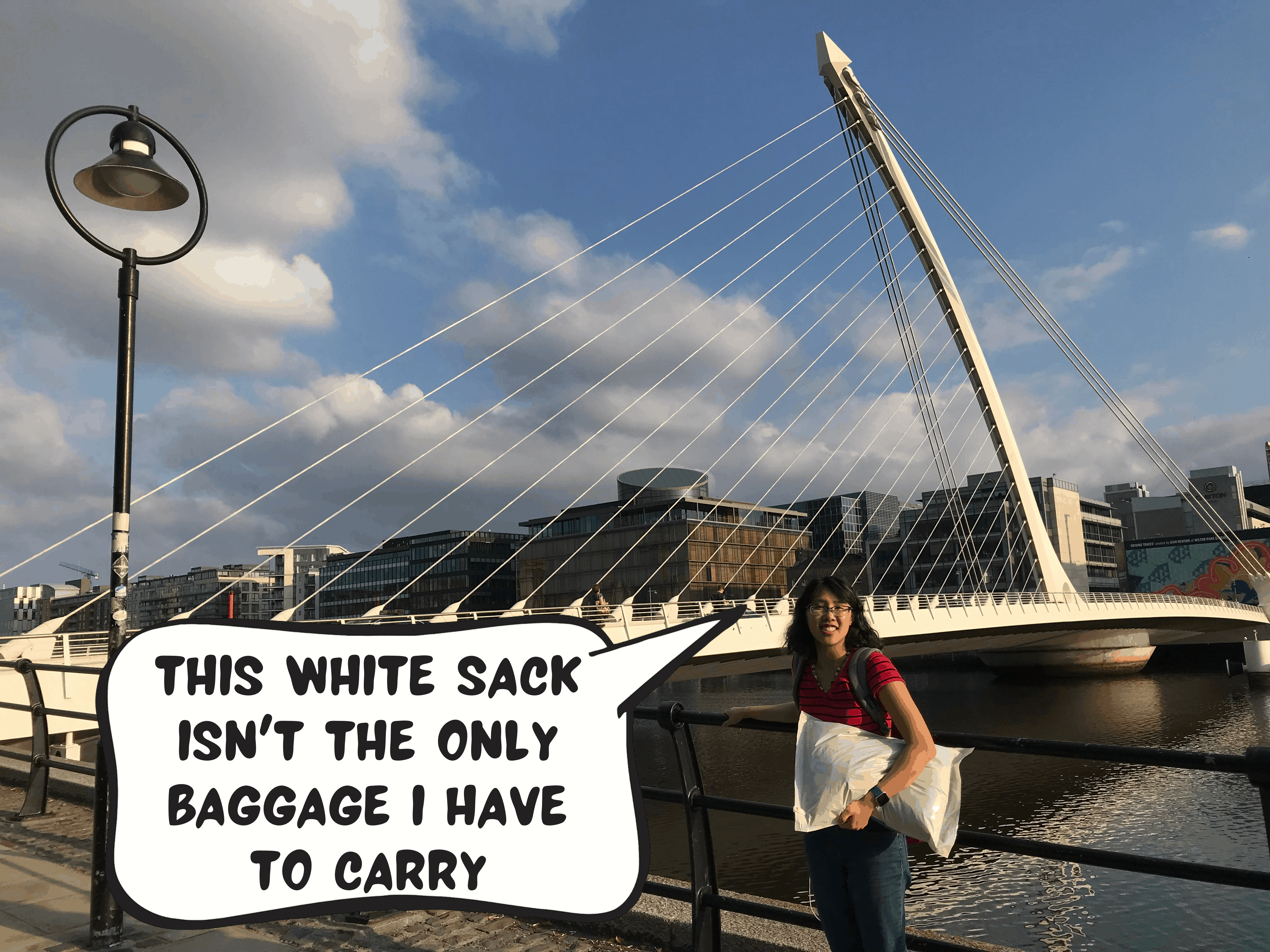 Meggie is wearing a black and red striped shirt as she is holding a white sack. She is standing in front of the Samuel Beckett white harp bridge in Dublin, Republic of Ireland. The bridge goes over the River Liffey. A blue sky with some clouds hangs over. Meggie, in a comic text box, says "this white sack isn't the only baggage i have to carry"