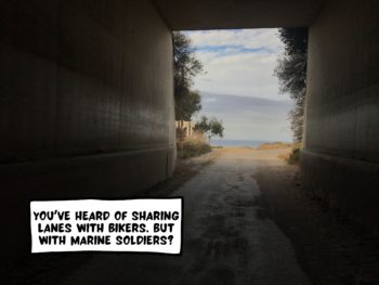 A dark tunnel. On the other end is the blue ocean and a cloudy sky. A bike trail runs through this pitch black tunnel. A comic text bubble says, "You've heard of sharing lanes with bikers. But with marine soldiers?" Las Pulgas/Old Pacific Highway Trail nearby Oceanside and San Clemente, California, United States of America