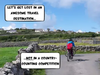 Meggie is biking on a countryside road surrounded by rolling green hills and gray cobblestone walls on Inisheer Island, in the Aran Islands in Galway Bay, Republic of Ireland, Europe. Blue sky with a few clouds. Village with homes perched on top of the huge hill in front.