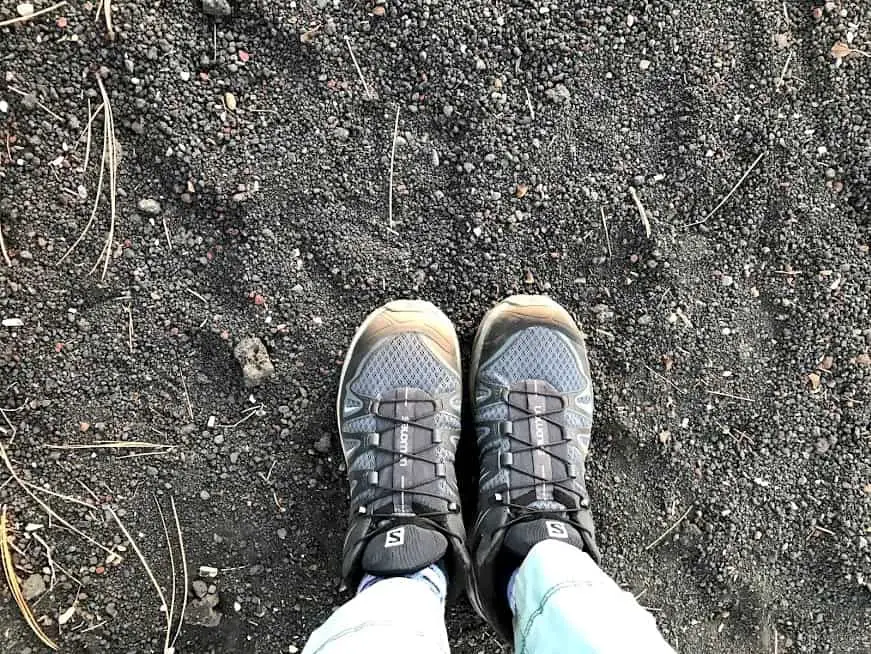 Meggie's gray hiking shoes over the ground of black ash rocks. Sunset Crater Volcano National Monument in Northern Arizona nearby Flagstaff, United States of America
