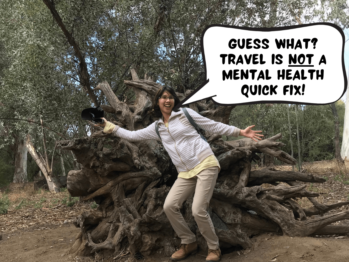 Meggie is standing with her arms wide open in front of a fallen tree with its roots upended. in a comic text bubble, she says, "guess what? travel is not a mental health quick fix!" In Boyce Thompson Arboretum State Park in Superior, Arizona, United States.