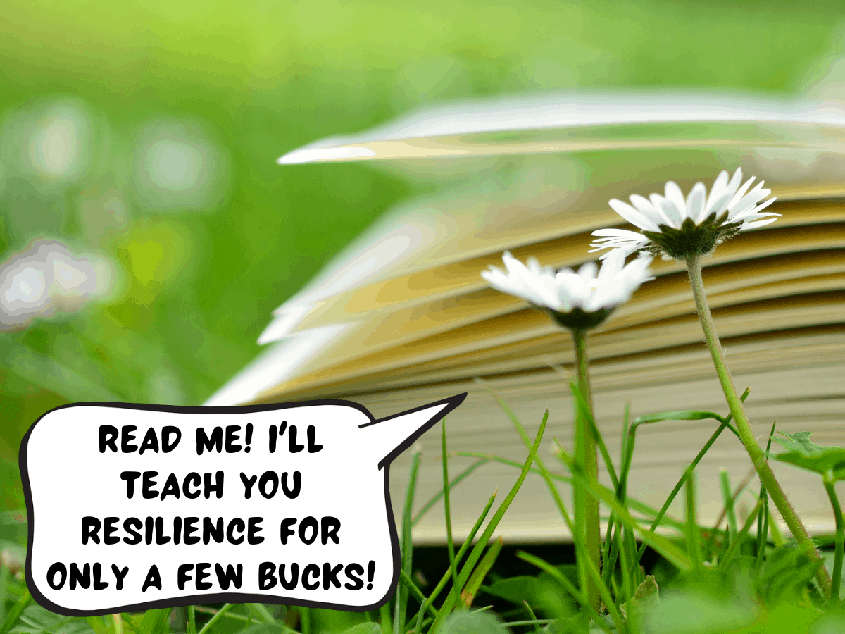 A book with white pages is lying in a grassy field with white flowers. The book is saying a comic text bubble, "read me! i'll teach you resilience for only a few bucks!"