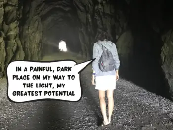 Meggie with her light blue jacket, backpack, and white shorts is walking through a dark cavernous tunnel, which used to have a railway. She is walking on gravel and towards the light at the end of the tunnel. She says in a comic text bubble, "In a painful dark place on my way to the light, my greatest potential." The Othello Tunnels in Hope, Fraser Valley, British Columbia, Canada.