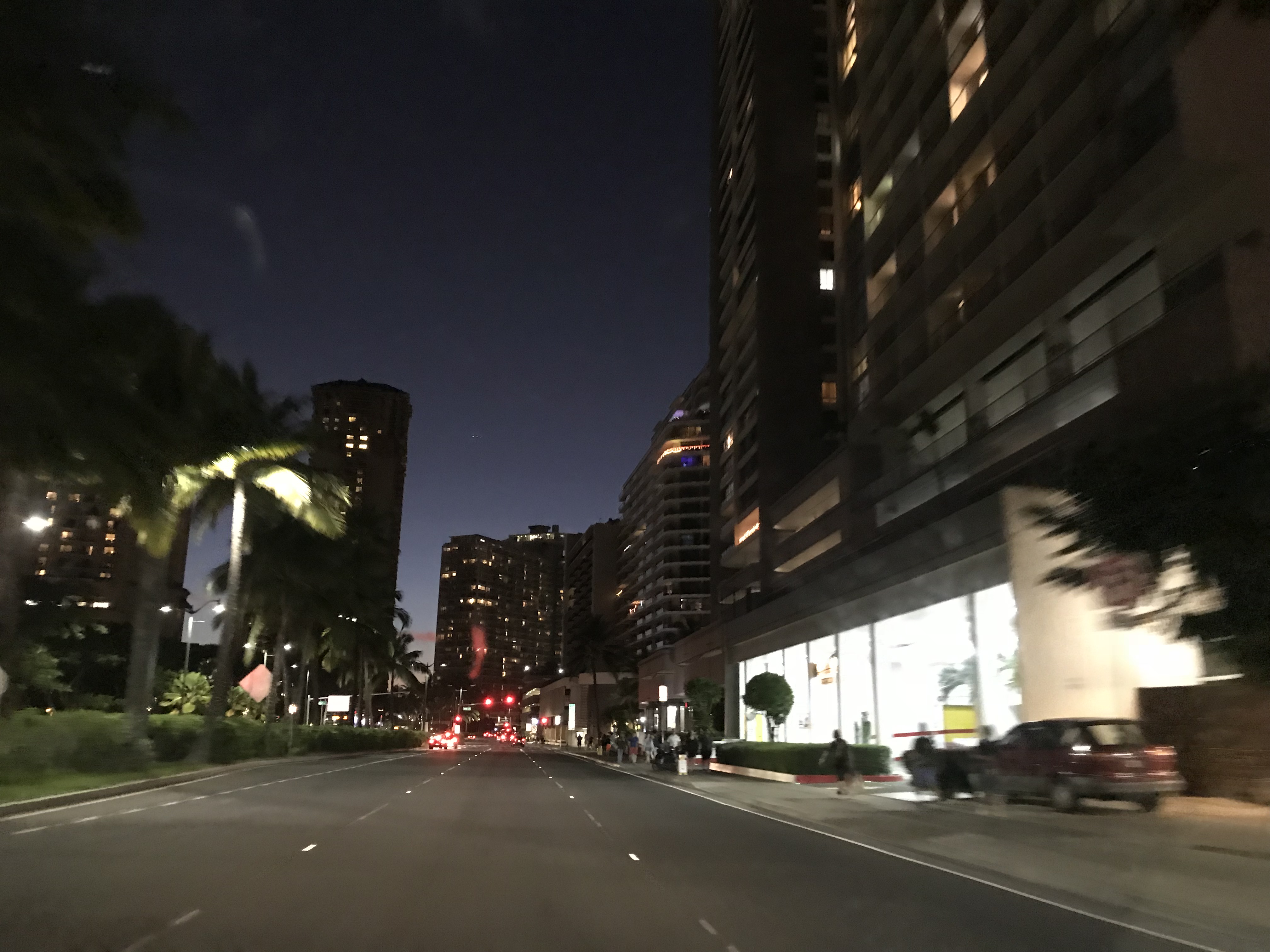 A car road with skyscrapers lining it. A nighttime scene in Downtown Honolulu, Hawaii, United States.