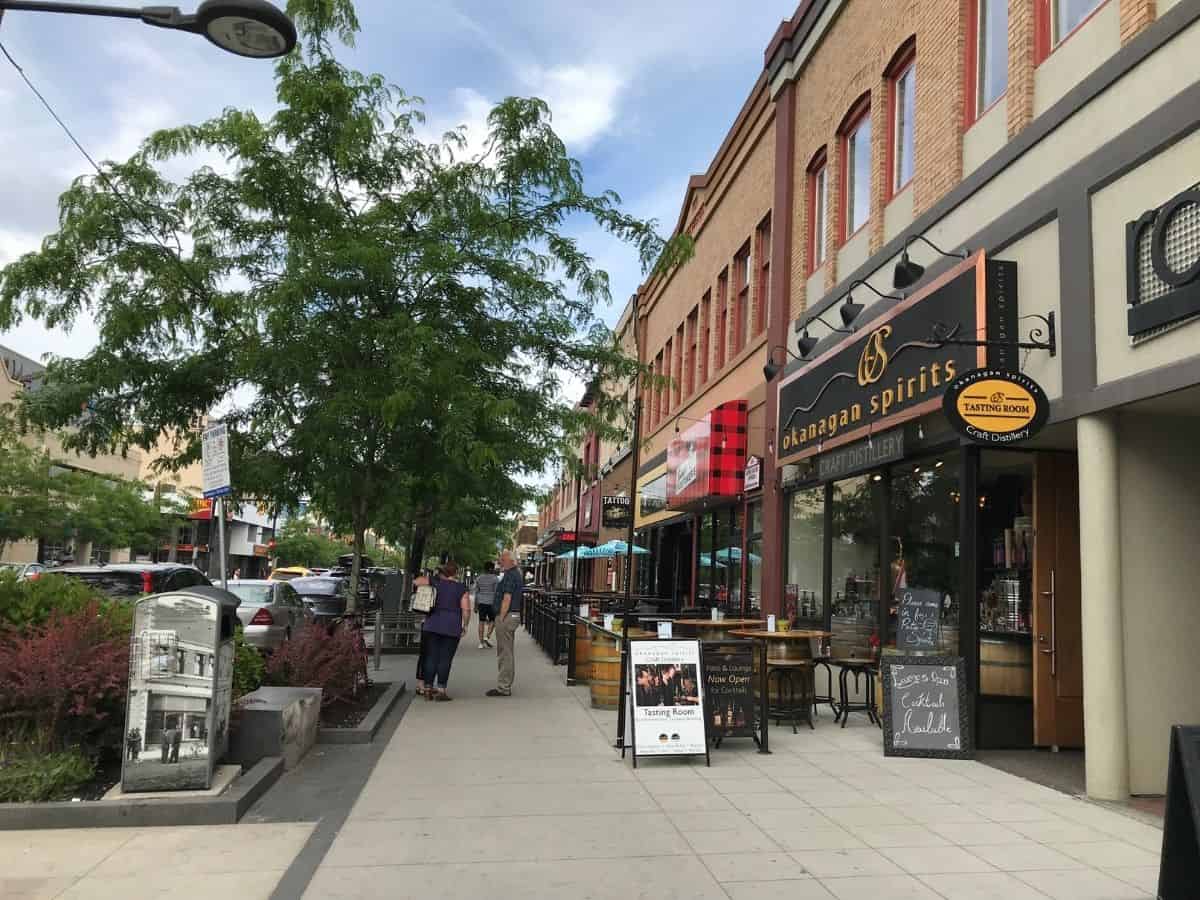 Eine Straße in der Innenstadt von Kelowna, British Columbia, Kanada, mit trendigen Geschäften der Mittelklasse, wie dem Okanagan Spirits. Von Bäumen gesäumt und von Ziegeln gesäumt