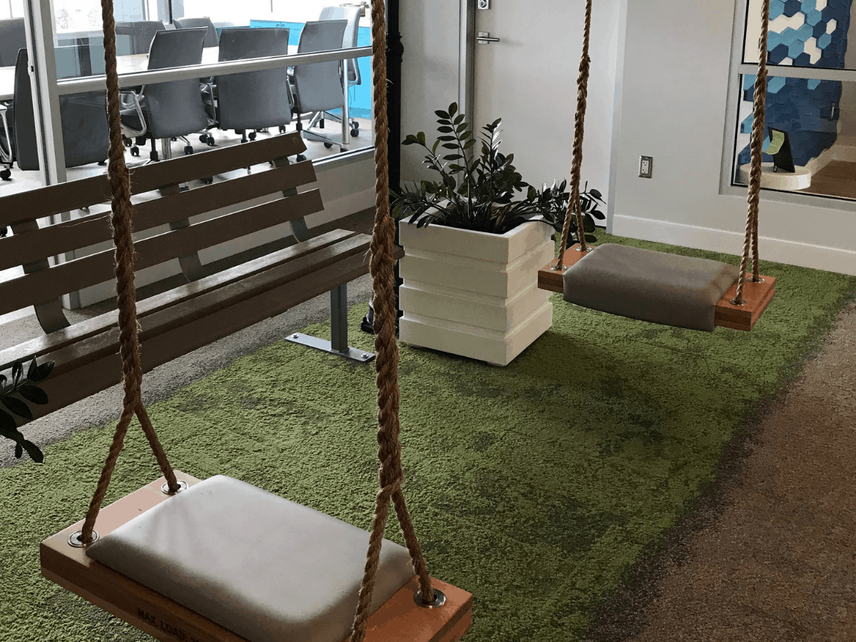 The FreshGrade office in the Okanagan Centre for Innovation in Kelowna, British Columbia, Canada. Two indoor swings over a green carpet. Behind the swings is an office conference room.