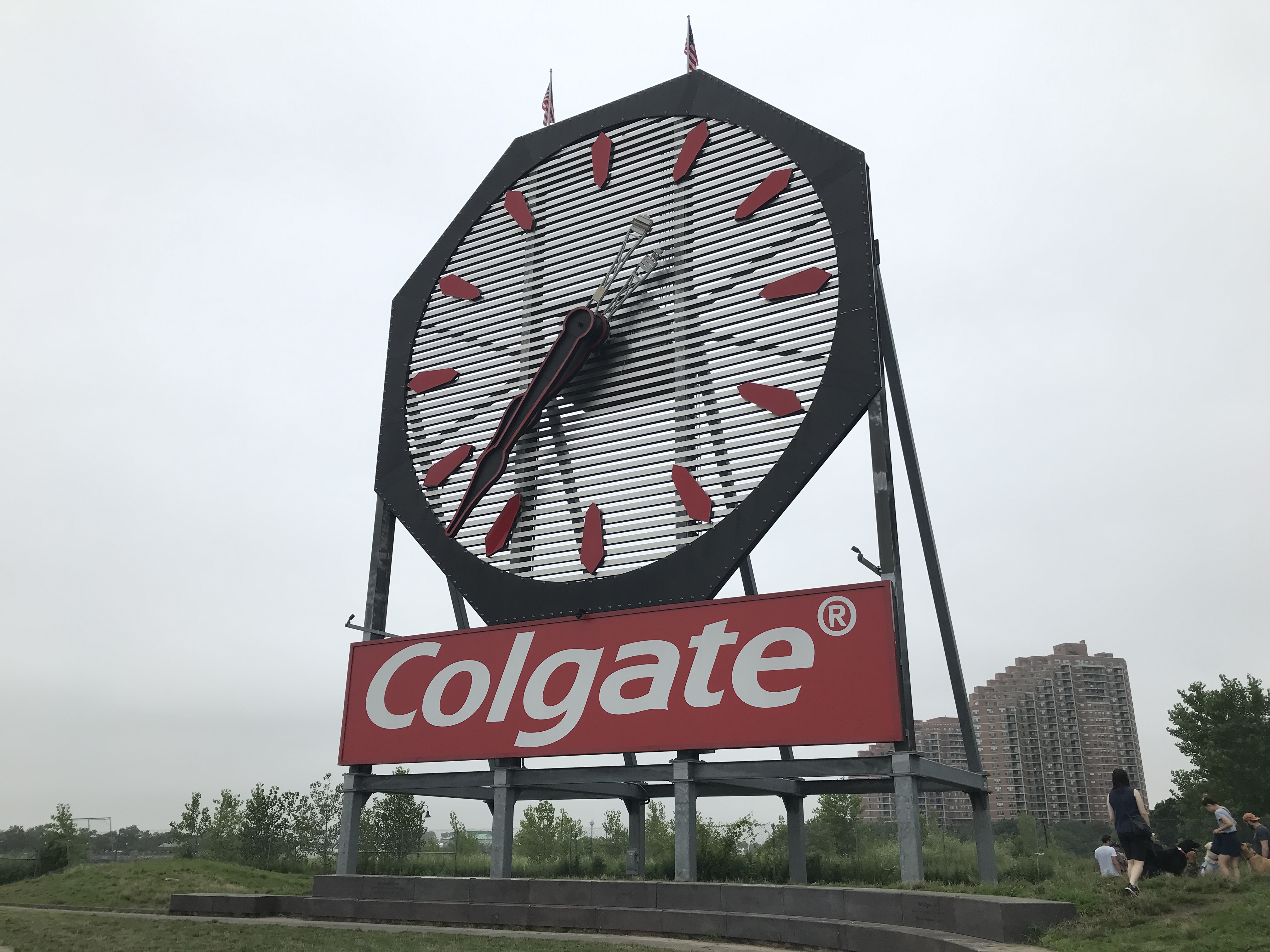 The red and white Colgate lettering logo is underneath the massive clock. The clock has red hour markings and black and red hands. Jersey City, New Jersey, United States. Sky is cloudy.