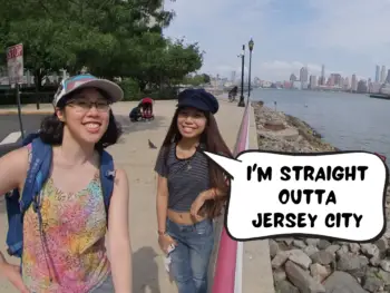 Meggie and their friend Athena are standing on the Jersey City Waterfront with the New York City skyline in the background. Athena says in a comic text speech bubble, "I'm straight outta Jersey City." Jersey City, New Jersey, United States