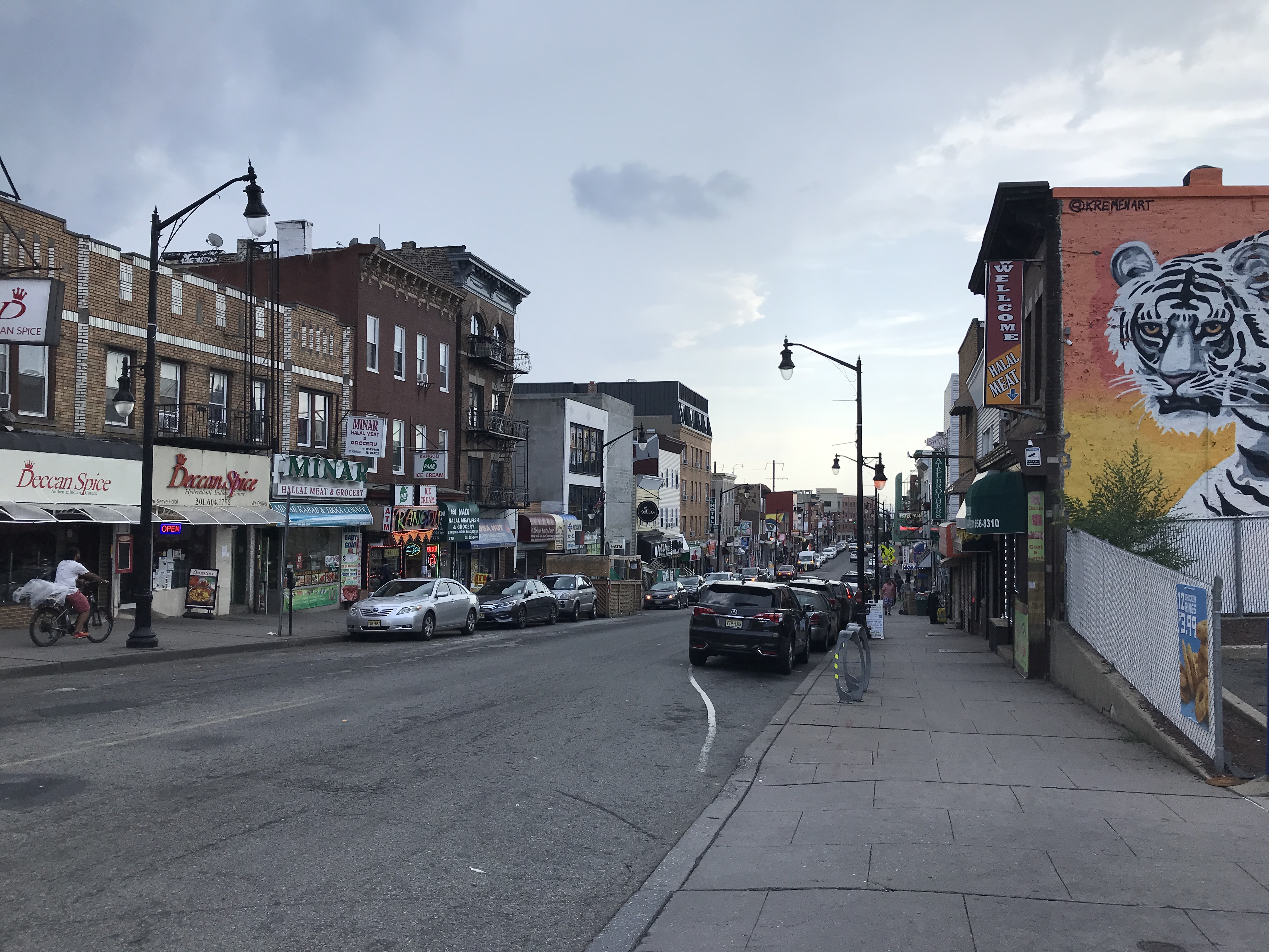 Looking down the sloping hill of India Square, with many Indian restaurants lining the street. A white Bengal tiger mural is painted on one of the building's sides. India Square, Journal Square, Jersey City, New Jersey, United States of America