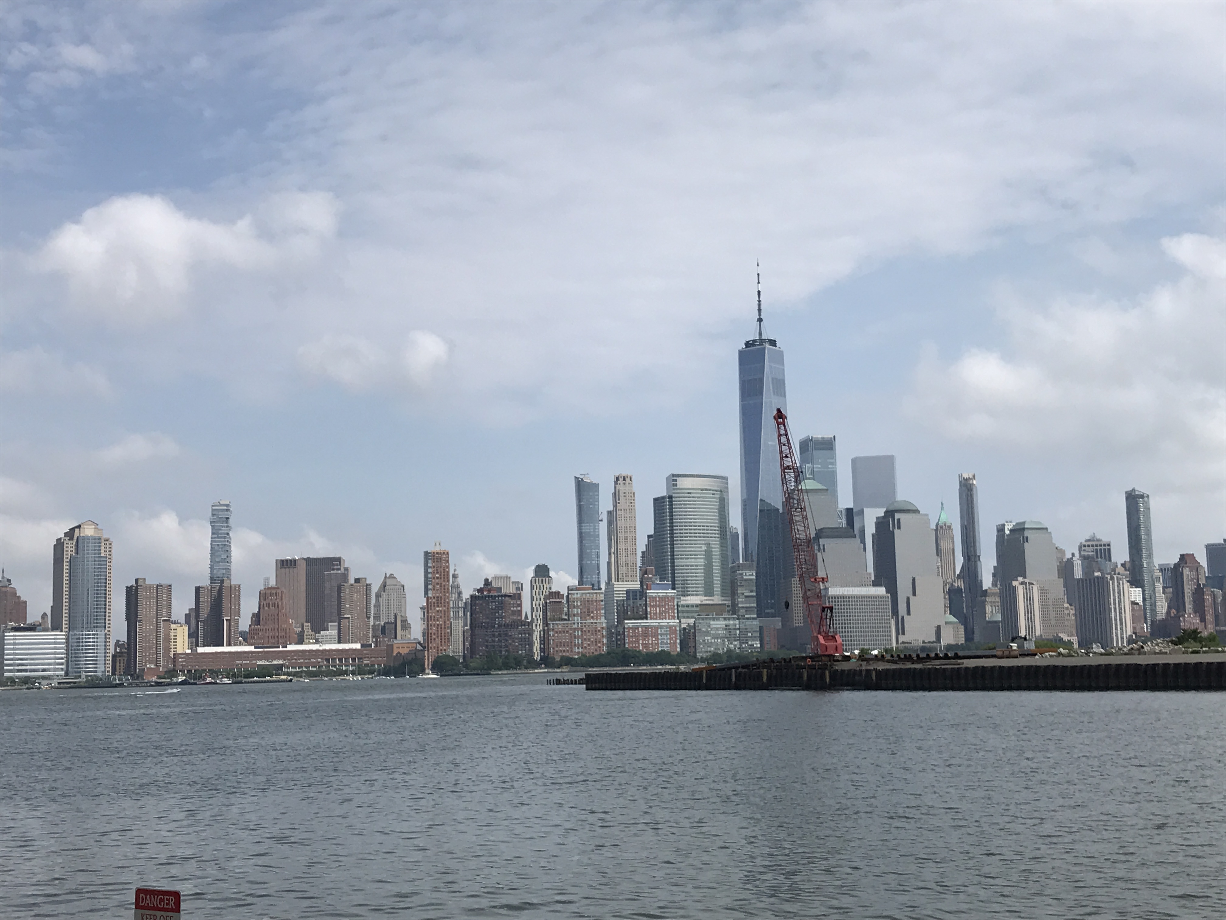 Views of the Downtown Manhattan cityscape with its tall skyscrapers, including the World Trade Center. Sky is party cloudy and blue. Jersey City, New Jersey, United States