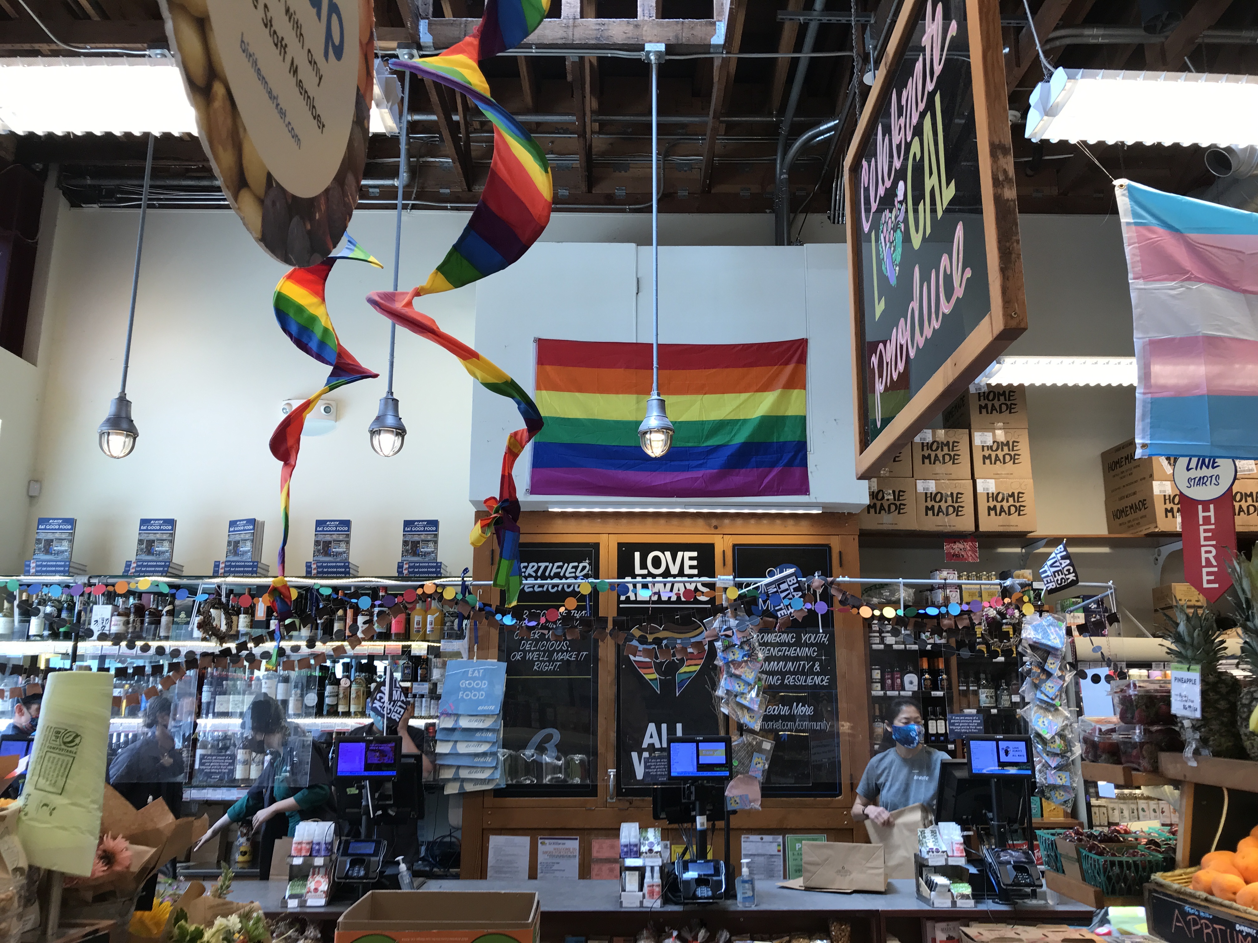 The interior of the Bi-Rite grocery store has rainbow streamers and flags, plus a light blue, light pink, and white transgender flag. Bi-Rite on Divisadero Street, San Francisco, California, United States of America