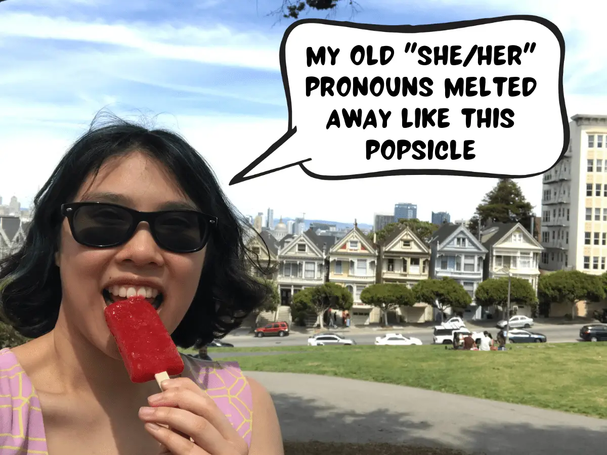 Meggie is eating a red popsicle, which is melting. They are standing in front of the Painted Ladies, a colorful row of houses. In a comic text speech bubble, Meggie says, "My old 'she/her' pronouns melted away like this popsicle." San Francisco, California, United States of America