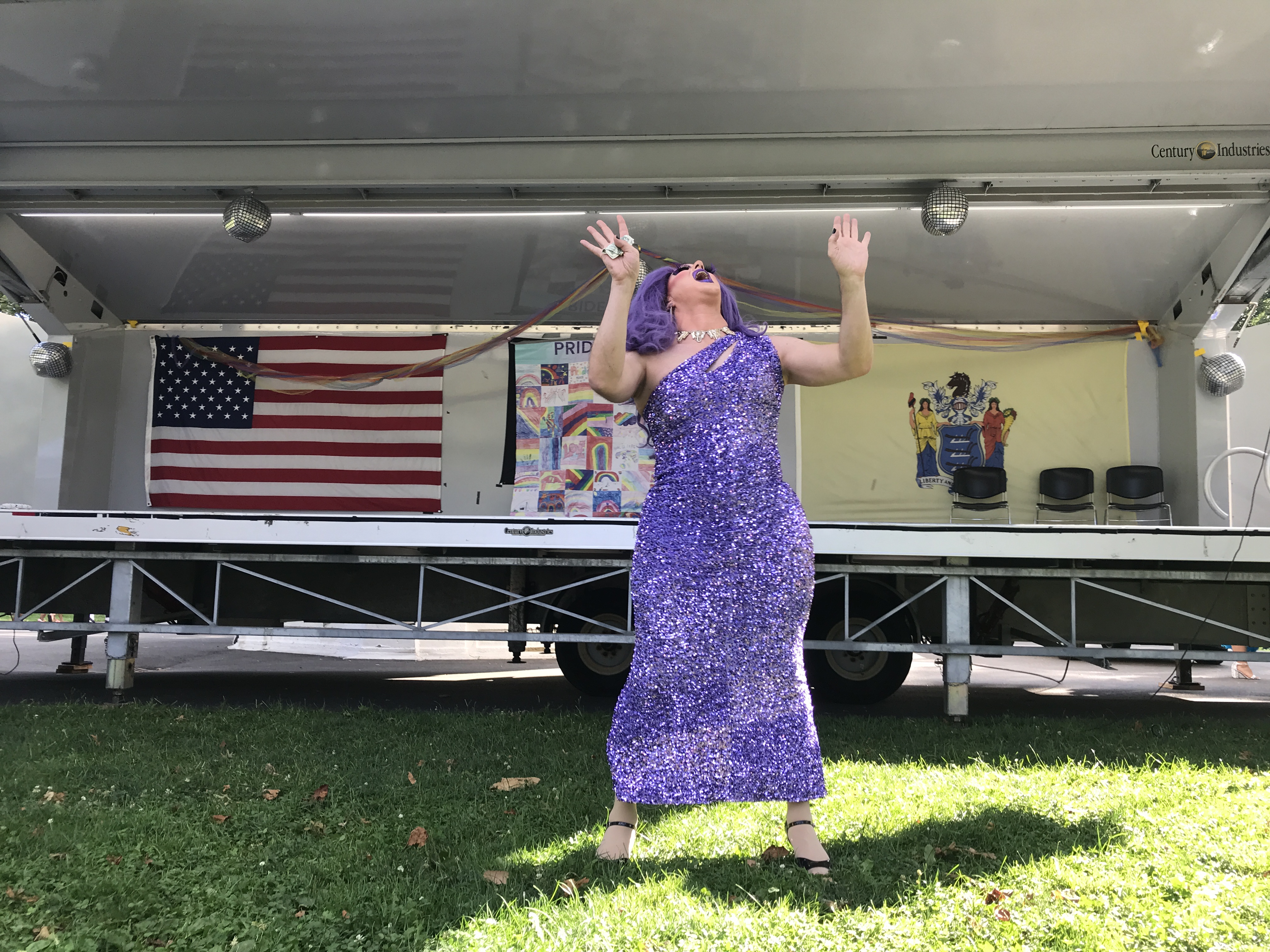 One of the drag show queens is wearing a sparkly purple dress and is dancing on the grass in front of the stage. Lincoln Park, Jersey City, New Jersey, United States of America