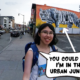 Meggie, wearing a white Levi's tank top, is standing on top of the sloping hill of India Square in front of a white Bengal tiger mural. Meggie, in a comic text speech bubble, says "You could say I'm in the urban jungle." India Square, Journal Square, Jersey City, New Jersey, United States of America