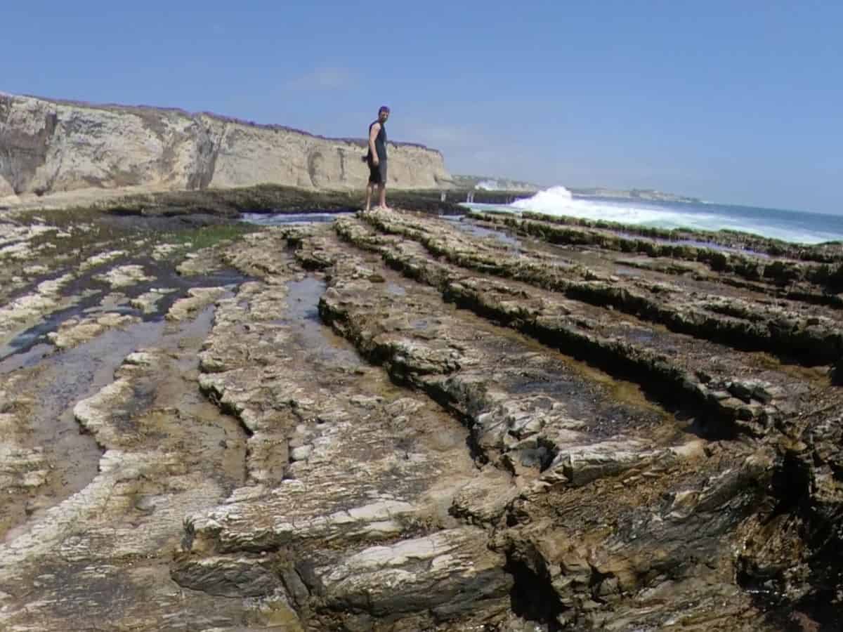 Naturally occurring rocky steps on the clifftop descending opposite from the oceanside. A large wave pounds in the background. Panther Beach, Santa Cruz, California, United States of America.