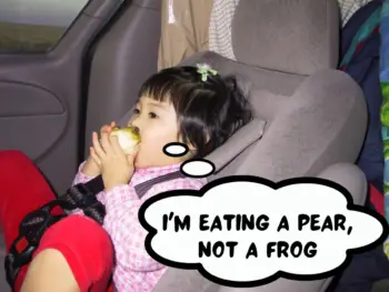 Baby Meggie is wearing a pink shirt and red pants as she's eating a peeled green pear in the seat of a van. Somewhere along Interstate-40, United States of America.
