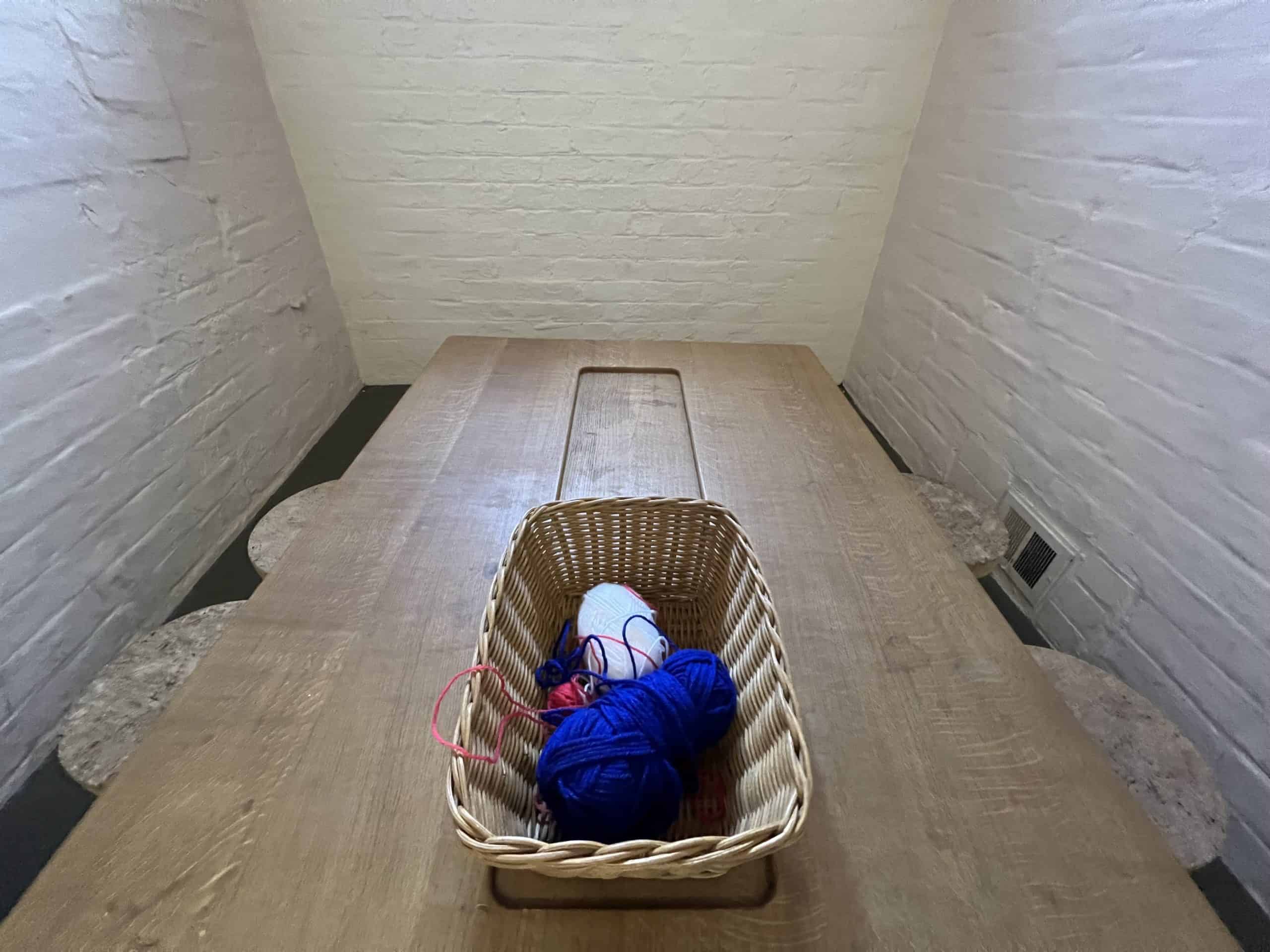 White brick walls in a prison cell. A wooden table with red, white, and blue yarn balls. On the grounds of Lincoln Castle, Lincoln, Lincolnshire, England, United Kingdom.