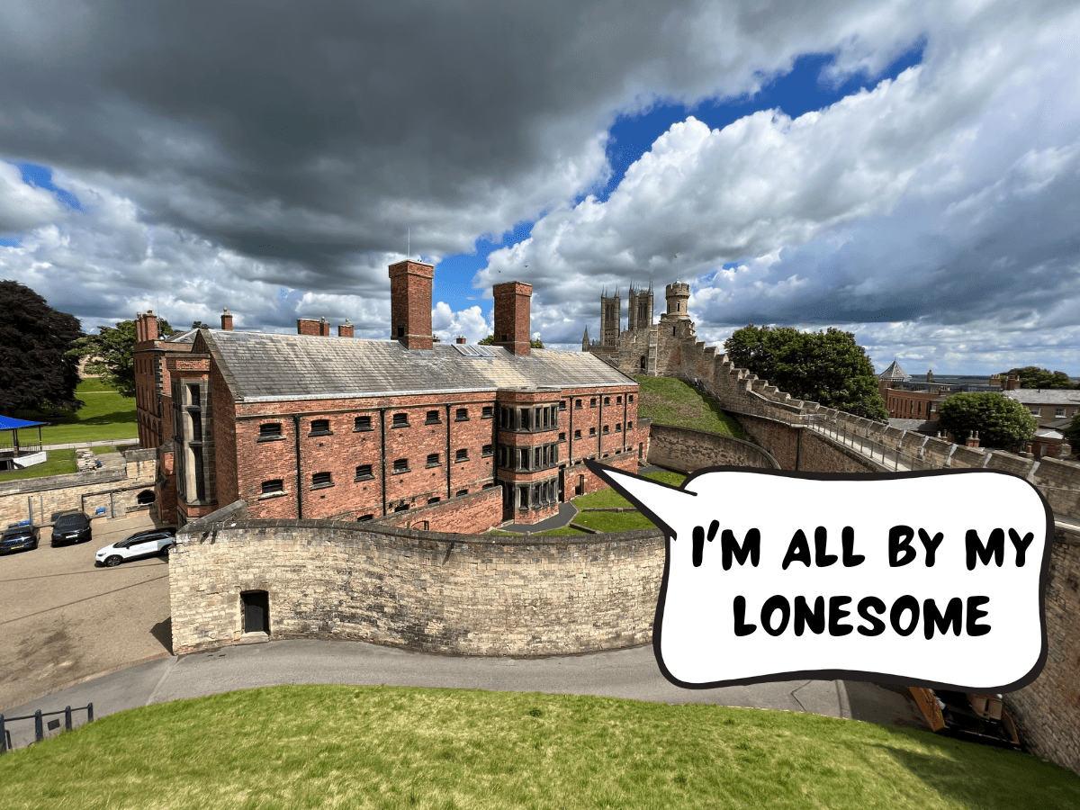 The red-bricked building of the Victorian-era prison. A comic text speech bubble is pointing to a window in the prison, saying, "I'm all by my lonesome." On the grounds of Lincoln Castle, Lincoln, Lincolnshire, England, United Kingdom.