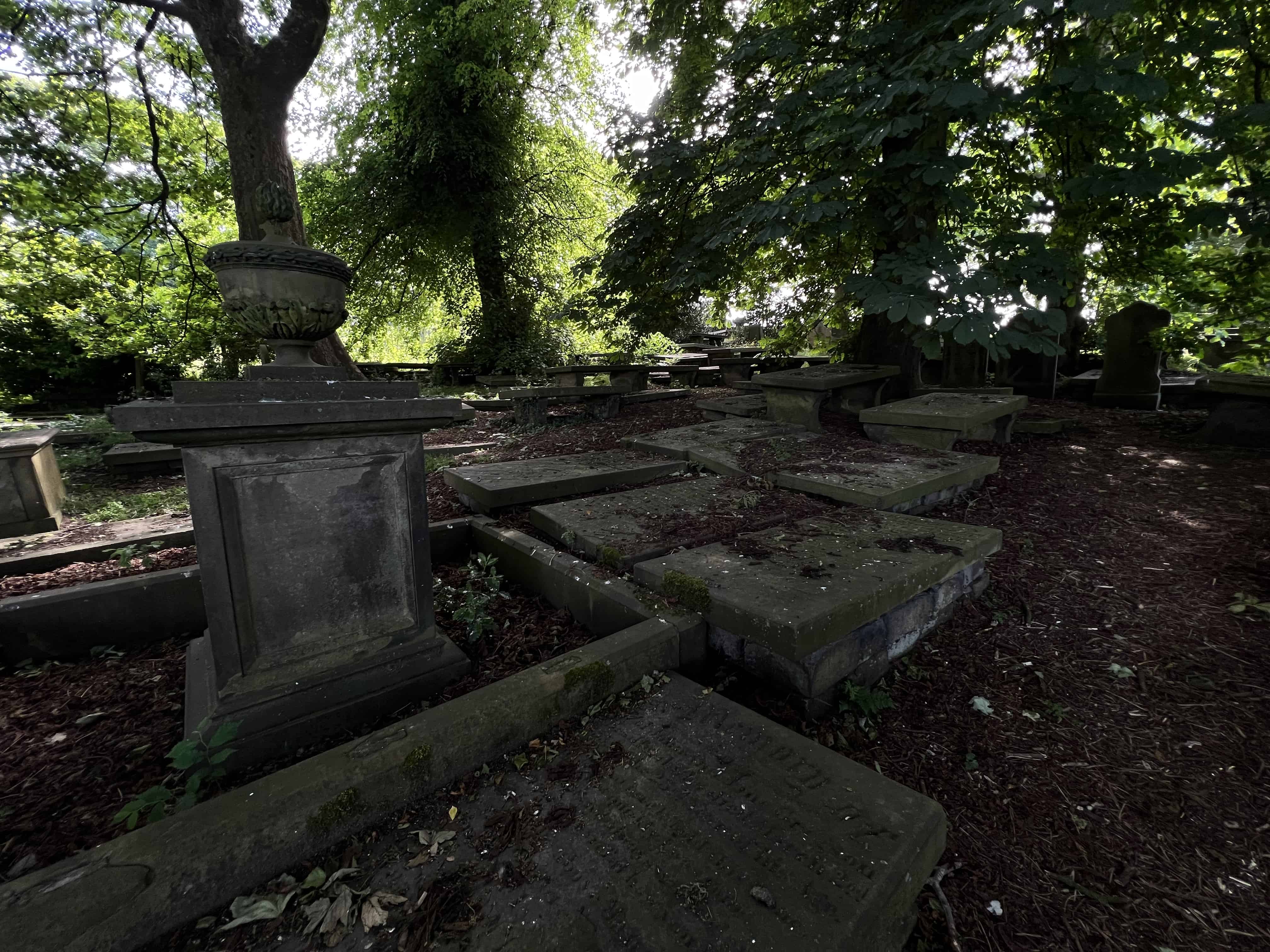 Flat tombstones are stacked on top of each other in the dark shadows of the trees overlooking the graveyard. St. Michael's Church, Haworth, Bradford, West Yorkshire, England, United Kingdom.