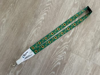 A green lanyard with yellow sunflowers rests on a grey wooden floor