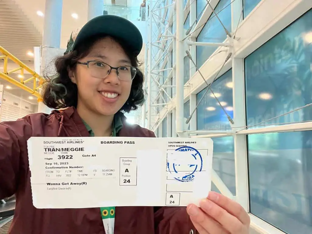 Meggie in a maroon jacket is holding up their Southwest boarding pass to Cuba at Fort Lauderdale airport.