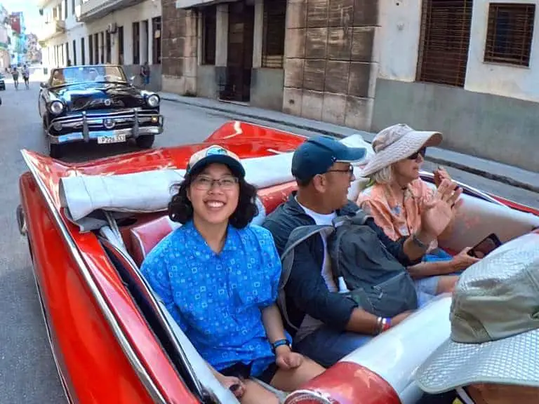 Meggie is wearing a blue shirt as they ride in a classic 1950s American car convertible in Havana, Cuba.