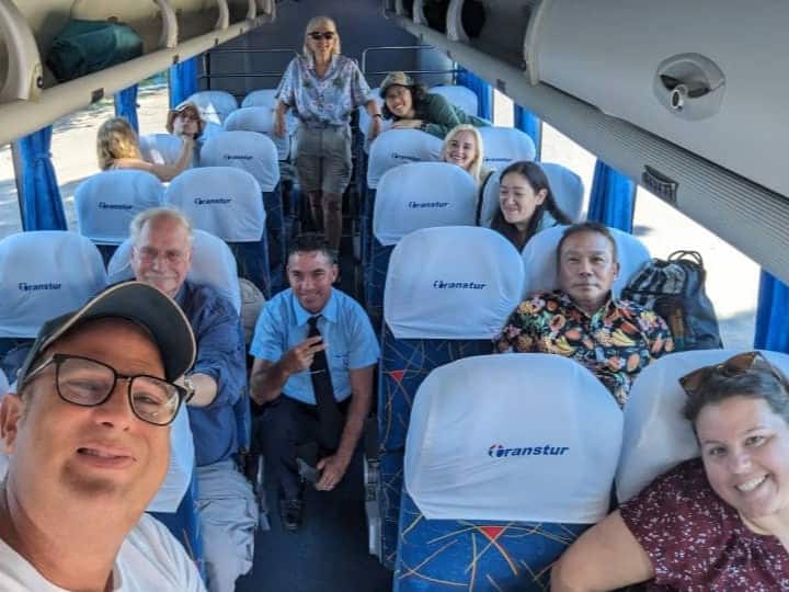 Meggie wearing a green shirt while inside the bus with their tour group, guide, and bus driver. The bus has blue seats with a white head covering.