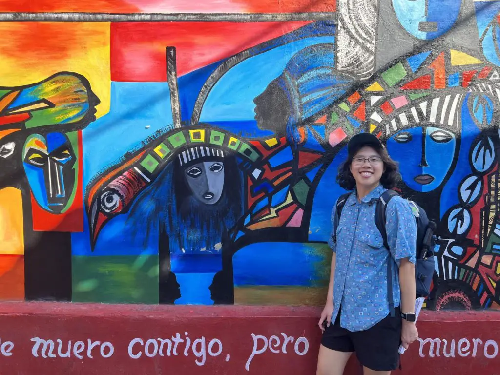 Meggie standing in front of Salvador's Santería-inspired mural with vibrant blue colors.