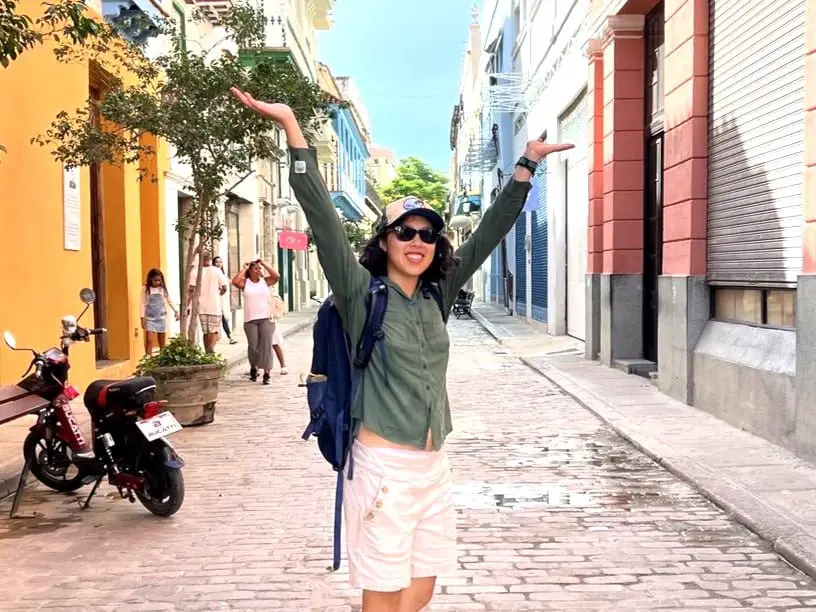 Meggie in a green shirt stands in the colorful yellow, red, and blue cobblestone streets of Havana, Cuba,