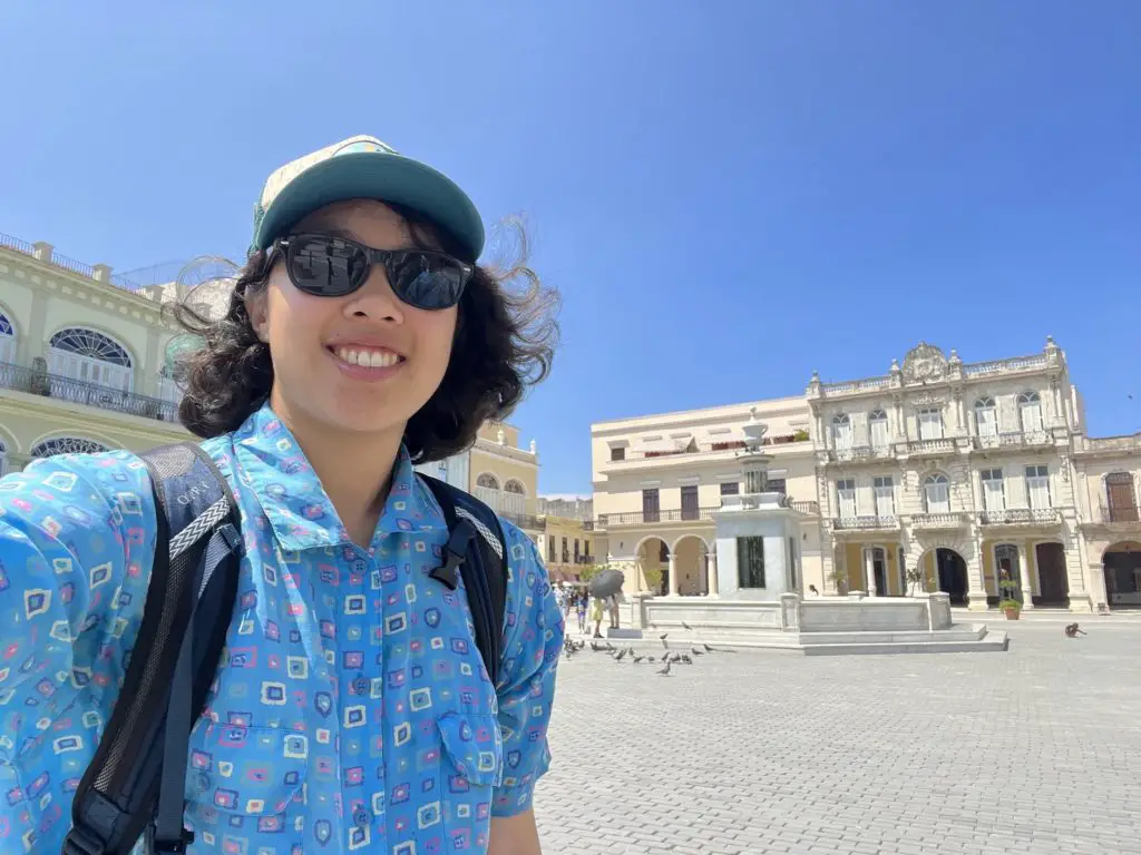 Meggie in a blue shirt standing in front of white-washed buildings in Plaza Vieja, Havana, Cuba.