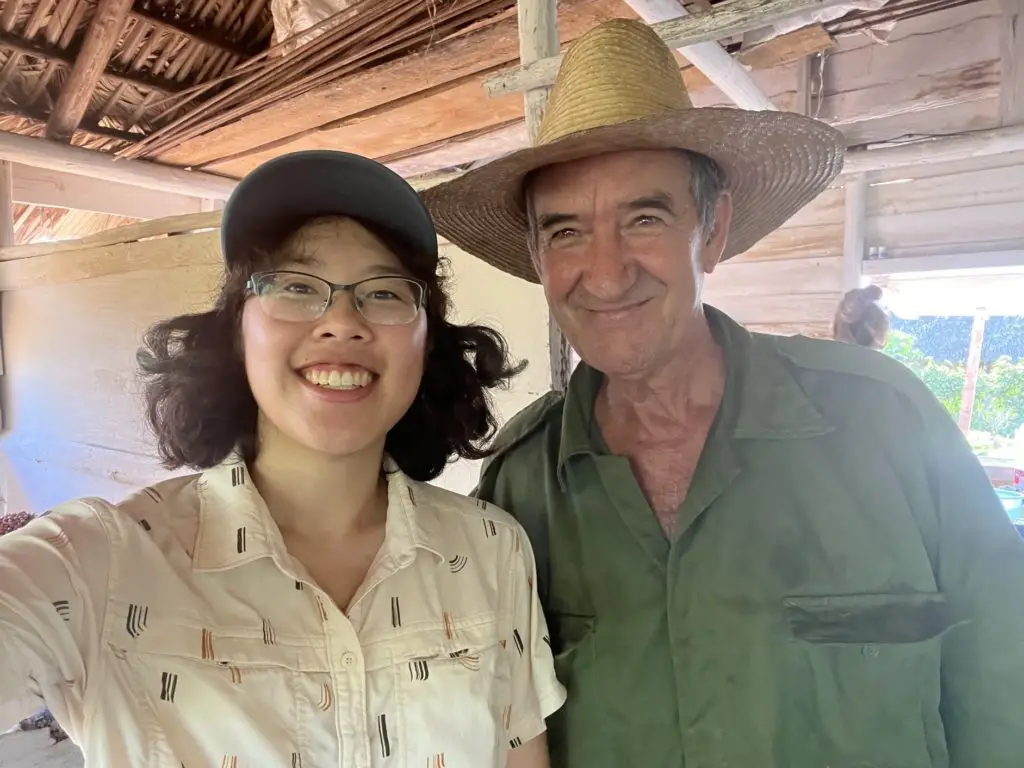 Meggie in a white shirt is taking a selfie with a Cuban farmer wearing a wide-brimmed hat and green clothes.