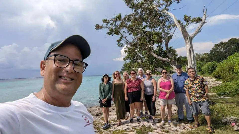 Meggie and their tour group standing on a rocky shoreline with crystal blue water of the ocean.