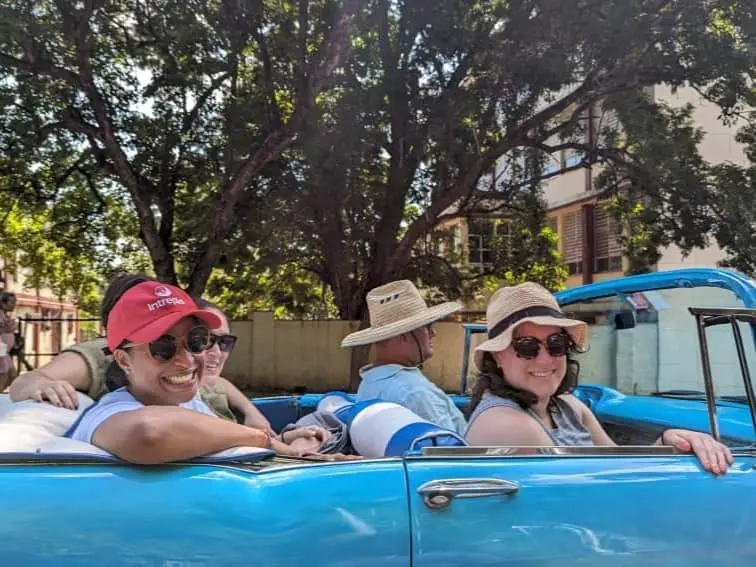 Diana, our Havana tour guide, wears a red Intrepid ball cap. She is sitting in a classic blue tour with my other tour mates.