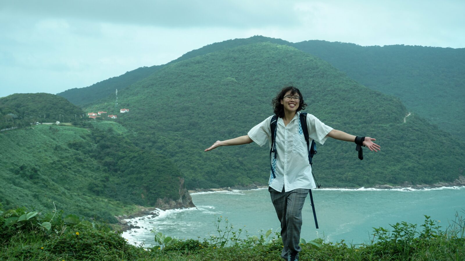 Meggie in a white shirt standing in front of the green forest and blue bay of Vietnam's Son Tra Peninsula.