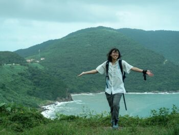 Meggie in a white shirt standing in front of the green forest and blue bay of Vietnam's Son Tra Peninsula.